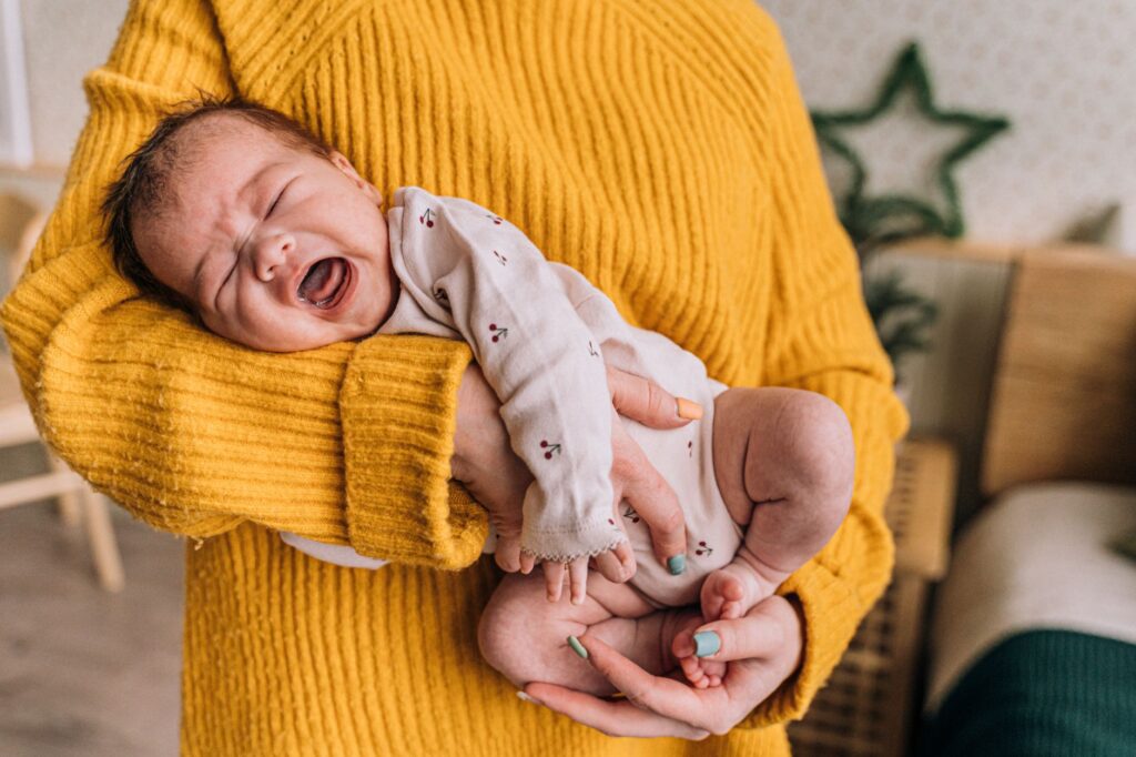 Exhausted parent holding a crying baby in a dimly lit nursery